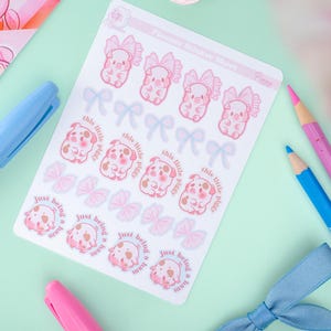 Puede incluir: Una hoja de pegatinas para planificador con ilustraciones de cerdos rosas con lazos y texto que dice "this little piggy" y "just being a ham". Las pegatinas est&aacute;n sobre un fondo blanco, con un fondo verde claro y rosa.