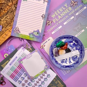 Könnte beinhalten: Ein Set an Frosch-Planer-Stickern und Notizblöcken mit einem lila und grünen Farbschema. Die Sticker zeigen einen Frosch mit einer Hexenmütze und Pilzen. Die Notizblöcke haben den Text "Hocus Croakus" aufgedruckt.