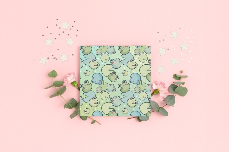 Puede incluir: Un papel de regalo estampado en verde y azul con un dise&ntilde;o repetido de ranas y nen&uacute;fares. El papel est&aacute; rodeado de peque&ntilde;as estrellas blancas y hojas verdes.