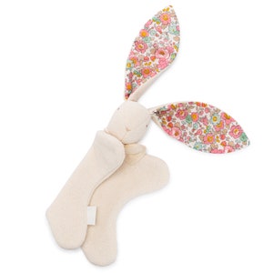 May include: A white plush bunny with floral print ears. The bunny is lying on its back with its arms and legs outstretched.