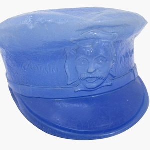 May include: A blue captain's hat with a brim and a detailed face of a man with a mustache. The word "CAPTAIN" is embossed on the hat. The hat is a gradient of light to dark blue.