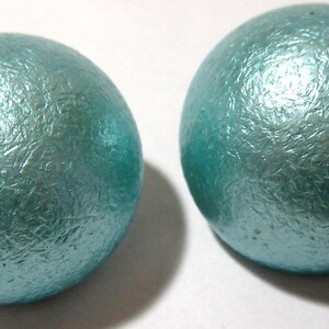 Op de afbeelding: Twee grote, ronde, turquoise oorbellen met een textuur en een metallic afwerking.