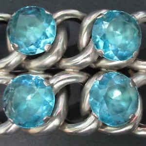 May include: A silver-toned bracelet featuring four oval, light blue gemstones. The gemstones are set within a chain-link design, creating a bold and elegant accessory. The bracelet's links are smooth and polished, reflecting light.