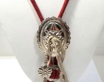 Könnte beinhalten: Ein rotes Bolo-Band mit einem silbernen Concho mit einem Sternmuster und einer Fransen aus Lederquasten.