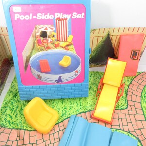 Pode incluir: Um brinquedo vintage "Pool-Side Play Set". O conjunto inclui uma moldura azul com fundo rosa, uma piscina e vários acessórios como uma cadeira amarela, um flutuador vermelho e uma espreguiçadeira amarela. O conjunto é projetado com um padrão de tijolos e um gramado verde.
