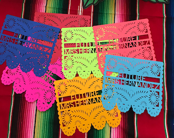 May include: A collection of colorful paper cutouts with the text "FUTURE MRS HERNANDEZ" in various colors, including blue, pink, red, yellow, and green. Large paper flowers in purple and blue are in the background, set against a striped textile.