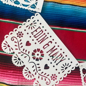 May include: White paper banner with a cut-out design, featuring the words "EDIN & MARY" in a decorative font. The banner is hanging against a colorful striped background.