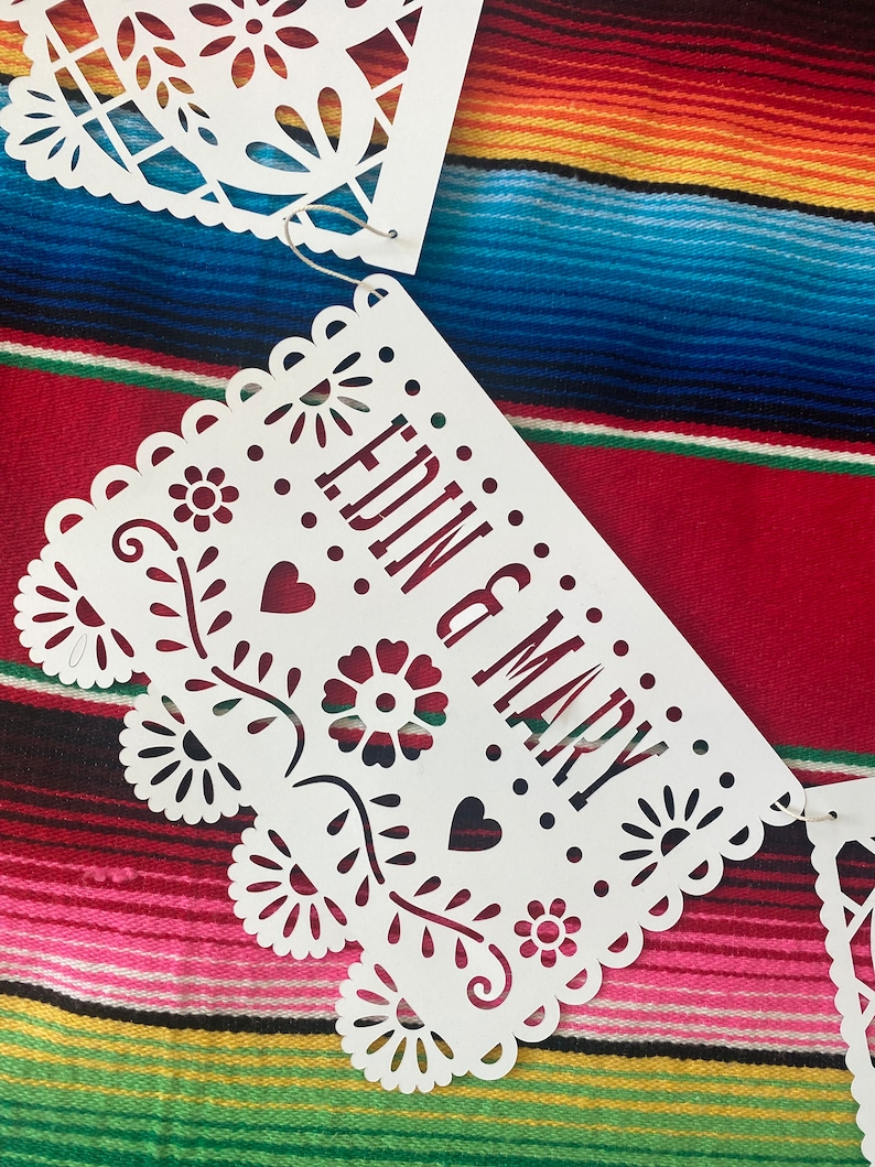 May include: White paper banner with a cut-out design, featuring the words "EDIN & MARY" in a decorative font. The banner is hanging against a colorful striped background.