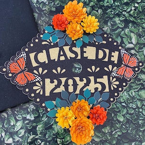 May include: Black graduation cap decorated with gold glitter, paper flowers in orange and yellow, and butterflies. The cap says "Class of 2025" in gold glitter.
