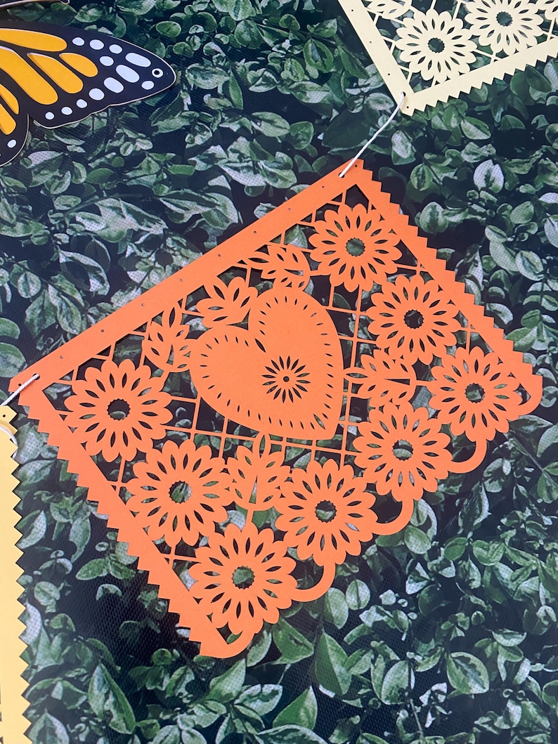 Puede incluir: Bandera de papel naranja con un coraz&oacute;n y dise&ntilde;os florales. La bandera est&aacute; recortada con detalles intrincados y tiene un borde festoneado.