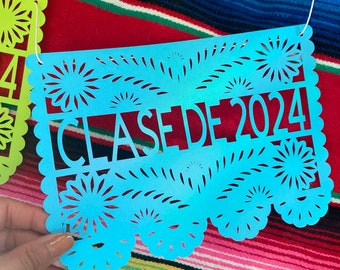 May include: A blue paper banner with a cut-out design of flowers and the text "CLASE DE 2024".
