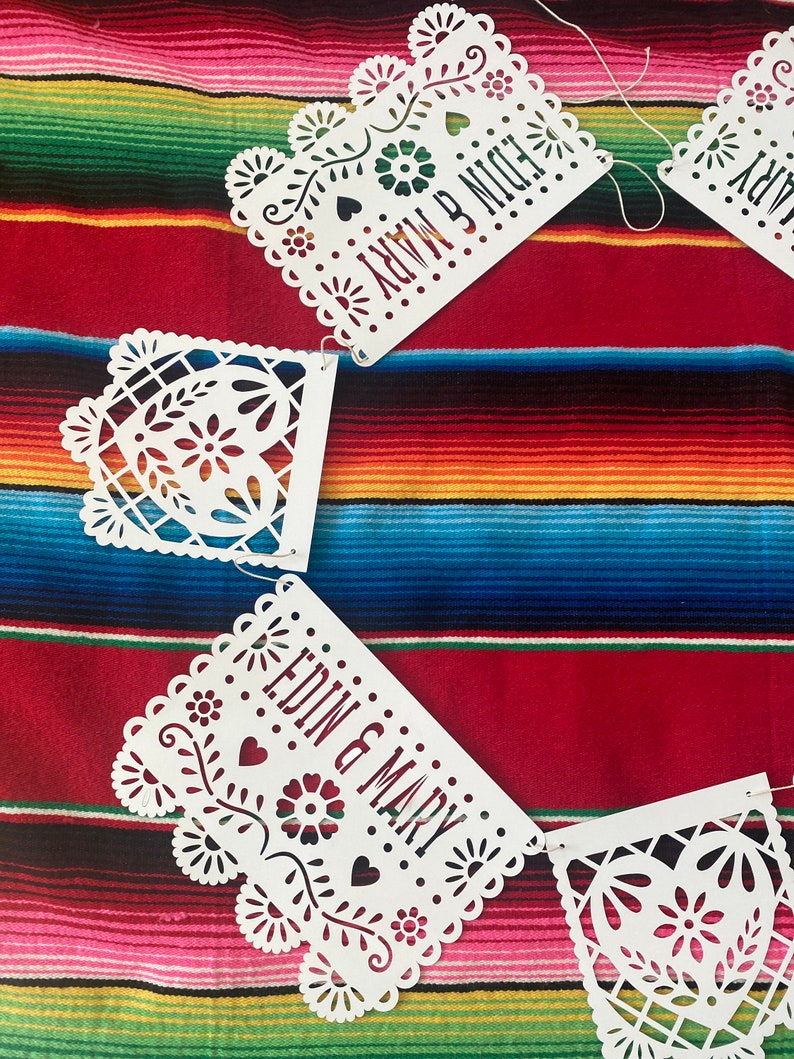 May include: White paper cut-out banner with the words "EDIN & MARY" and "NOW & NIGHT" on a colorful striped background.