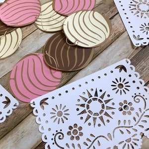 May include: A white paper garland with cut-out designs of flowers and a sun. The garland is strung with brown, pink, and white paper circles.