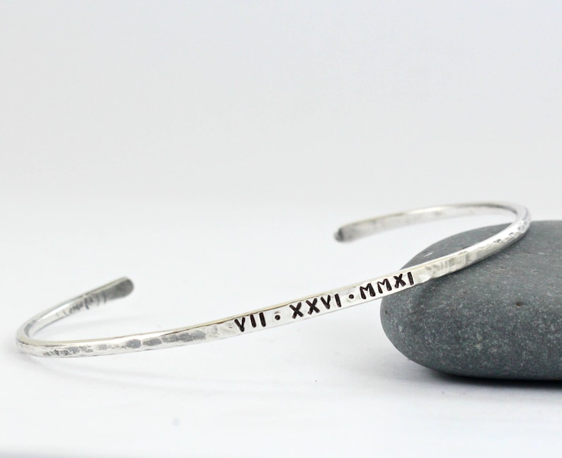 May include: A silver hammered bangle bracelet inscribed with the date "VIII. XXVI. MMXI".