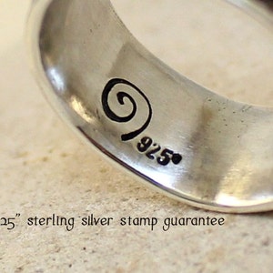May include: Close-up of a silver ring with a swirl design and the marking "925" on the inside band.
