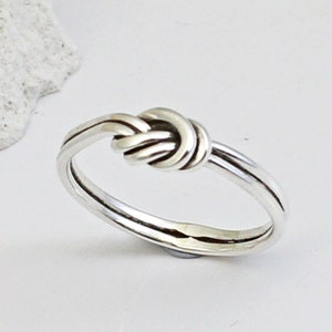 May include: A silver knot ring with a simple, elegant design. The ring is made from a single piece of metal that is twisted and knotted to create a unique and eye-catching look.