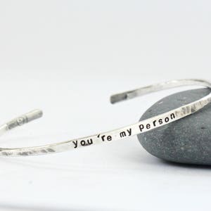 May include: A silver hammered bangle bracelet inscribed with the words "You're my person".