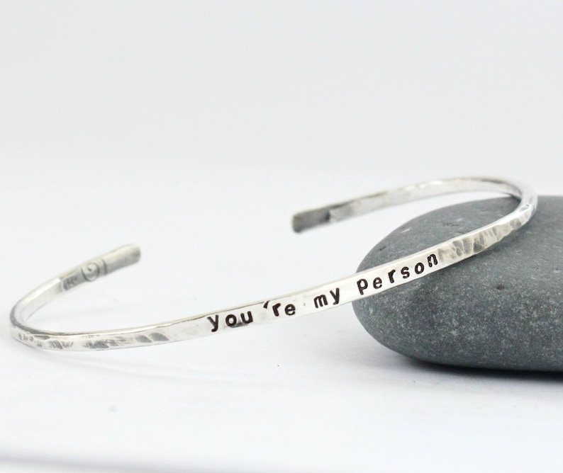 May include: A silver hammered bangle bracelet inscribed with the words "You're my person".