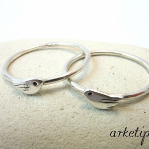 Könnte beinhalten: Zwei silberne Ringe mit einem Vogelmotiv. Die Ringe sind schlicht und elegant, und das Vogelmotiv ist zart und charmant.