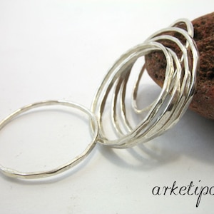 May include: A silver pendant necklace featuring multiple textured oval rings connected together. The design includes a single, smaller ring attached to the larger cluster. The word "arketipo" is written in a script font.