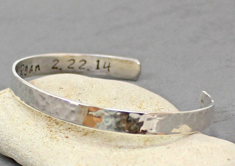 Op de afbeelding: Een zilveren gehammerde armband met de inscriptie "Ryan 2.22.14" gegraveerd aan de binnenkant.