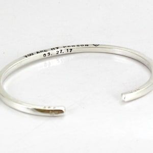 May include: Silver bangle bracelet with the inscription "You are my person 03.27.17" engraved on the outside.