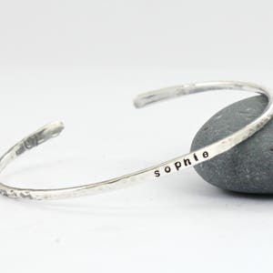 May include: A silver hammered bangle bracelet engraved with the name "Sophie".