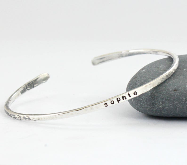 May include: A silver hammered bangle bracelet engraved with the name "Sophie".