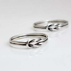 Op de afbeelding: Twee zilveren ringen met een knoopdesign. De ringen zijn simpel en elegant.