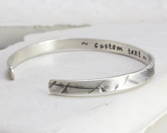 Może przedstawiać: Srebrna bransoletka typu bangle z fakturowaną powierzchnią i napisem "~ custom text ~".