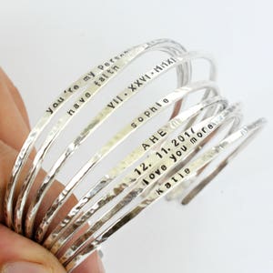 May include: A set of seven silver bangle bracelets with personalised inscriptions. The inscriptions include "You're my person", "have faith", "VIII. XXVI. MMXI", "sophie", "AHE", "12. 11. 2017", "love you more", and "katie".