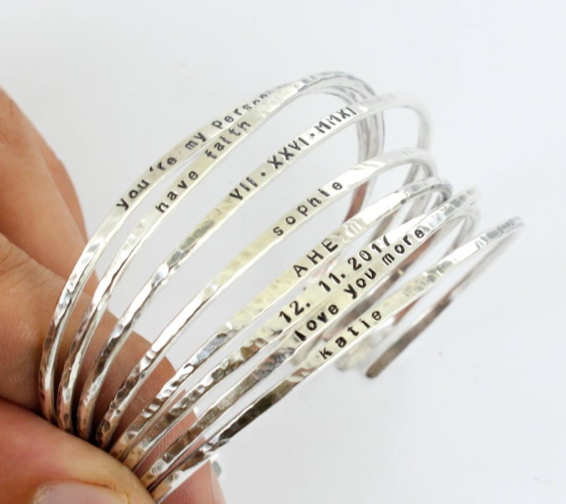 May include: A set of seven silver bangle bracelets with personalised inscriptions. The inscriptions include "You're my person", "have faith", "VIII. XXVI. MMXI", "sophie", "AHE", "12. 11. 2017", "love you more", and "katie".