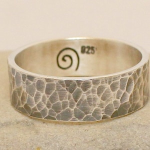 Op de afbeelding: Een zilveren gehammerde bandring met een swirl-ontwerp en de inscriptie "925" aan de binnenkant.
