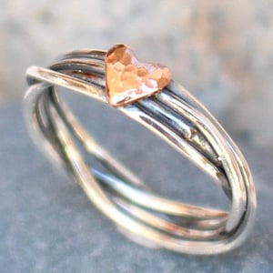May include: A silver ring with a hammered copper heart design. The ring is made of three intertwined bands.