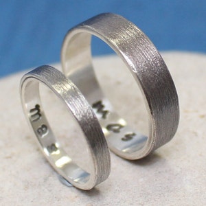 Op de afbeelding: Twee zilveren trouwringen met een geborstelde afwerking. De ringen zijn gegraveerd met de initialen "M & S".