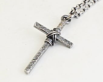 Könnte beinhalten: Eine silberne Kreuzkette mit einem strukturierten Design und einem verdrehten Drahtdetail. Die Kette ist eine silberne Panzerkette.