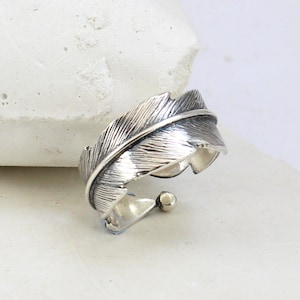Op de afbeelding: Een zilveren ring met een gedetailleerd veren ontwerp. De ring is verstelbaar en heeft een gladde, gepolijste afwerking.