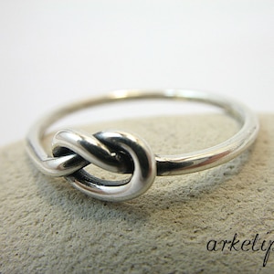 May include: A silver ring with a knot design. The knot is a simple, elegant design that is perfect for everyday wear.
