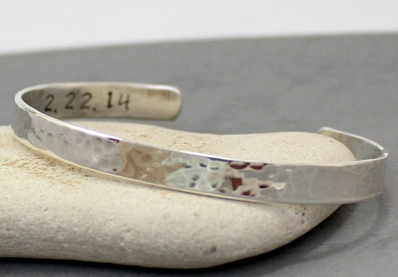 Op de afbeelding: Een zilveren gehammerde armband met de datum "2.22.14" gegraveerd aan de binnenkant.