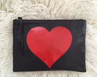 Bolsa con cremallera de cuero en piel de color negro con corazón pintado en rojo.