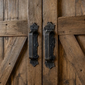 Peut inclure: Deux poignées en métal sombre et texturé montées sur une paire de portes en bois verticales. Les portes présentent une finition en bois brun patiné avec des planches de renfort diagonales. Les poignées ont une finition noire mate martelée.