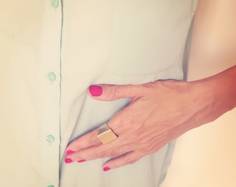 May include: A person wearing a light blue button-down shirt with a gold ring on their finger.