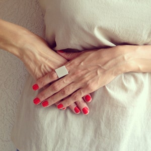 Puede incluir: Una mano de mujer con un anillo rectangular blanco y esmalte de uñas rojo.