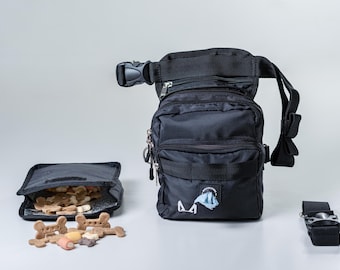May include: Black nylon dog waste bag holder with a zippered pocket and a detachable strap. The bag holder is filled with dog treats and a blue tissue.