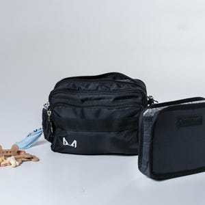 May include: A black fanny pack with a zippered pocket and a small, black, zippered pouch. The fanny pack has a white "M" logo on the front.
