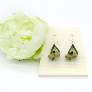 May include: A pair of olive green ribbon earrings with silver hooks. The earrings are tied in a knot and hang from the hooks.