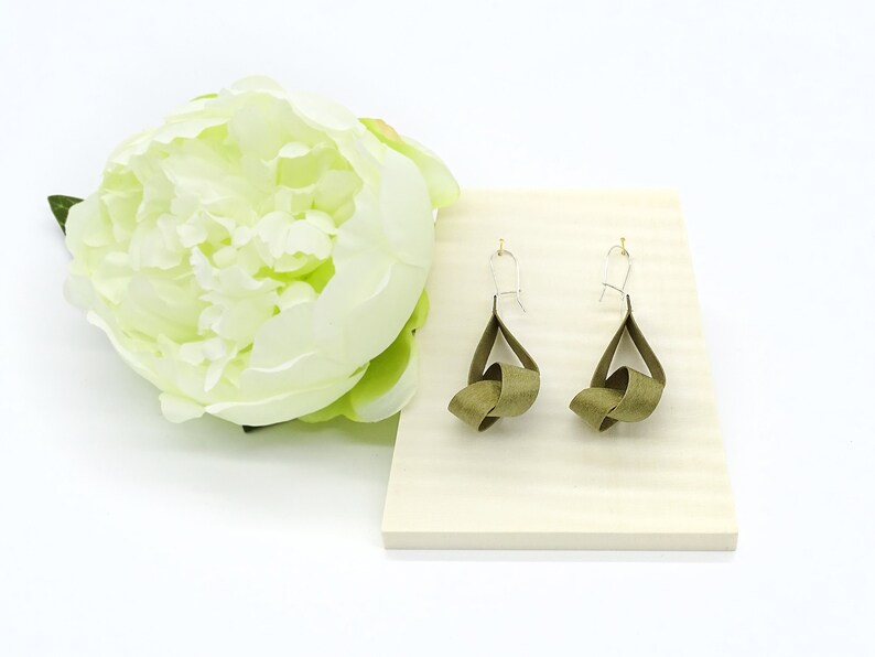 May include: A pair of olive green ribbon earrings with silver hooks. The earrings are tied in a knot and hang from the hooks.