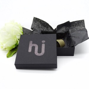 May include: A black gift box with the word "hi" printed in silver on the top. The box is open and filled with black tissue paper.