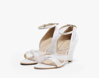 Può includere: Scarpe da sposa in raso bianco con un design in pizzo e un tacco a zeppa. Le scarpe hanno un dettaglio a fiocco sul davanti e un cinturino alla caviglia con chiusura a fibbia.