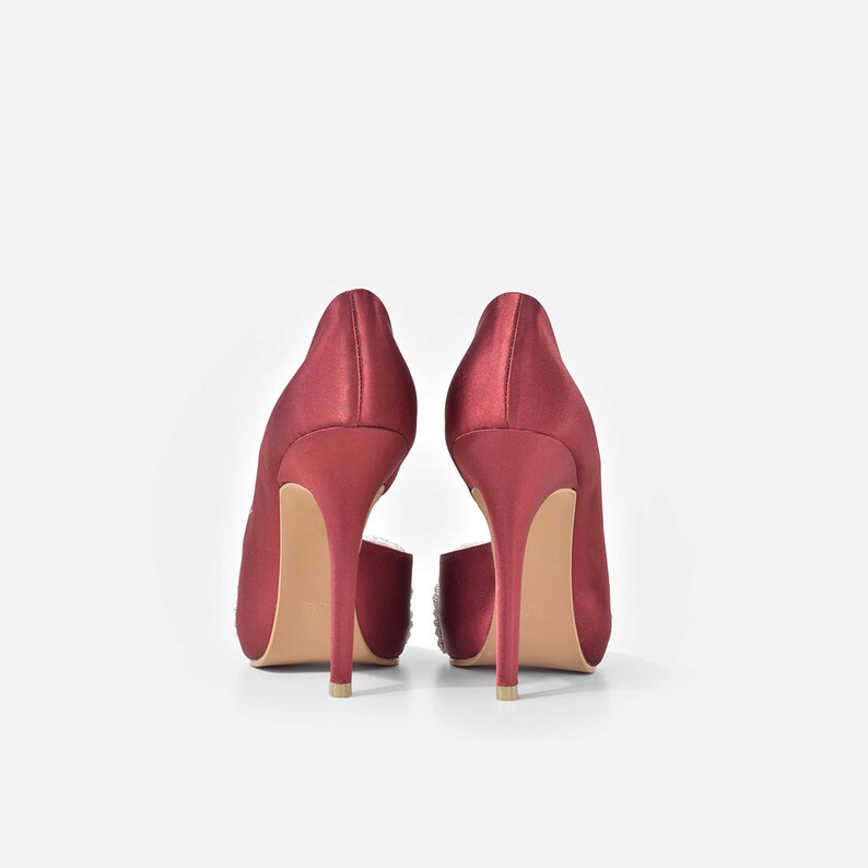 May include: A pair of burgundy satin high heels with a peep toe and a small embellishment on the back of each shoe.